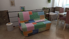 Ein farbenfrohes, gestreiftes Sofa in einem Raum mit Fliesenboden, einem kleinen Mülleimer und einem Tisch mit Stühlen.