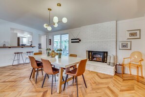 Ein moderner Essbereich mit Kamin aus weißem Backstein, Holzparkett in Fischgrätmuster und einem großen Tisch mit Stühlen.