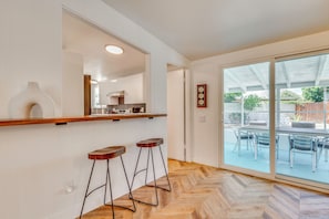 Eine Küche mit Holzarbeitsplatte, zwei Barhocker, einem großen Fenster und einer Glastür zu einer Außenpatio.