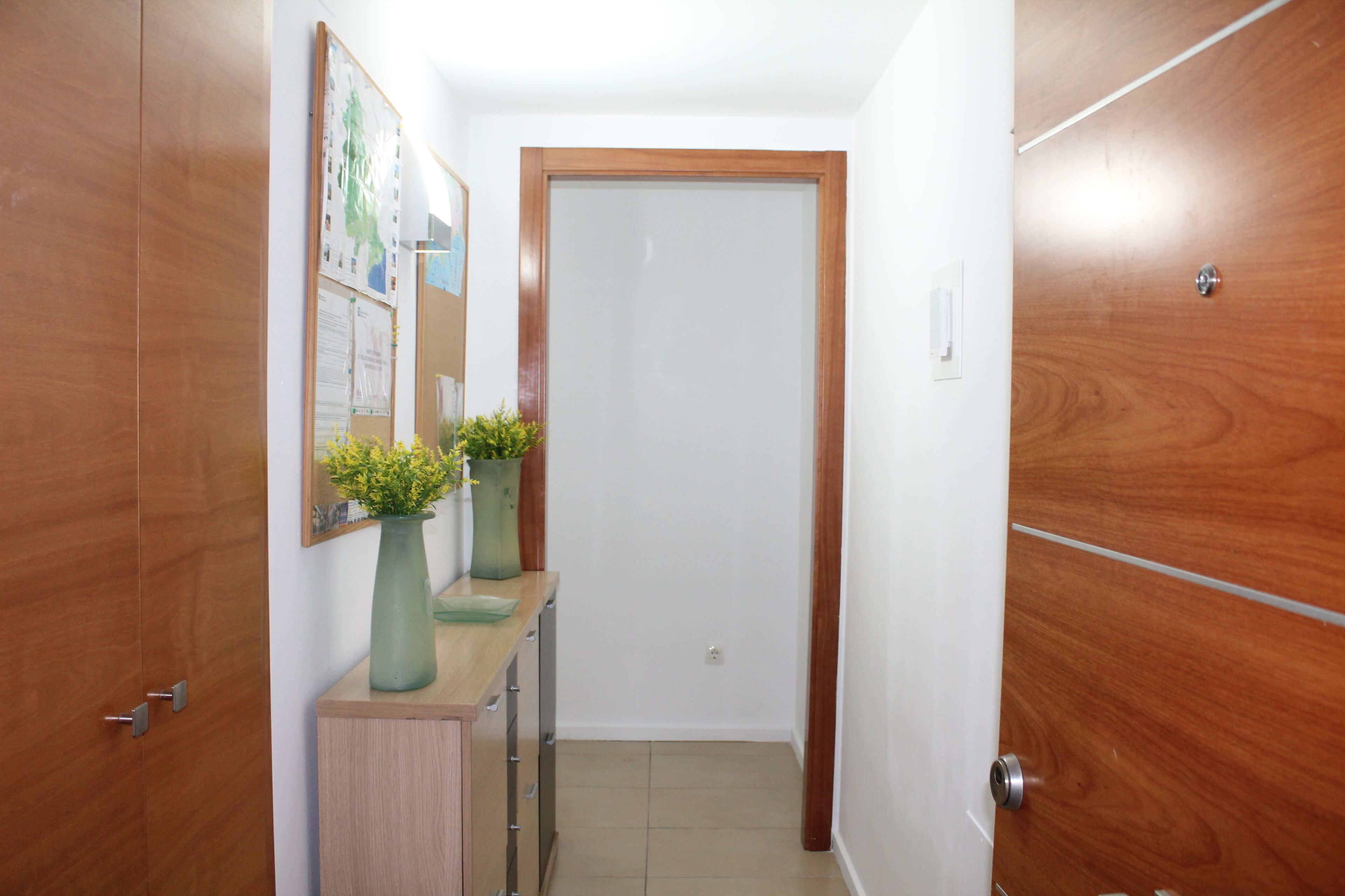 Un pasillo con puertas de madera, un pequeño mostrador con un florero y un cuadro en la pared.