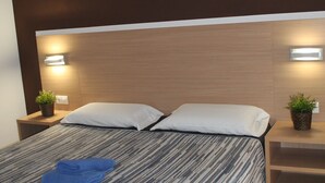 Quarto de hotel com uma cama, duas mesas de cabeceira e luminárias fixadas na parede.