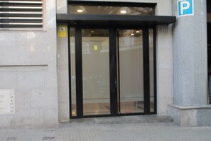 Une entrée d’immeuble avec une porte en verre, un panneau indiquant l’emplacement du parking et une plaque numérotée.