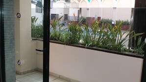 Visão através de uma janela com barreira de plantas, uma porta com um aviso e um chão de azulejos.