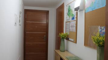 Un couloir avec une porte en bois, un tableau d’affichage orné de cartes et un petit bureau sur lequel se trouve un vase.