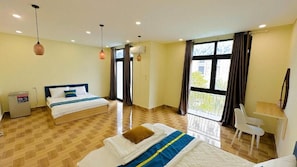 Quarto de hotel com duas camas, uma escrivaninha, uma cadeira e janelas amplas.