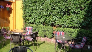 An outdoor patio with a round table and chairs, surrounded by a hedge and a wooden fence. - Maria Apartment 2 – Stay in the Heart of Wernigerode (Wernigerode)