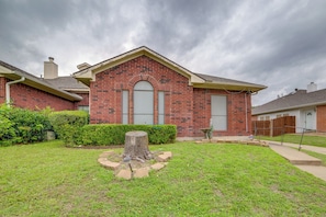 A residential building with a brick facade, a front yard with a tree stump, and a wooden fence. - Extended DFW Retreat w/ Private Patio & Grill (Garland)