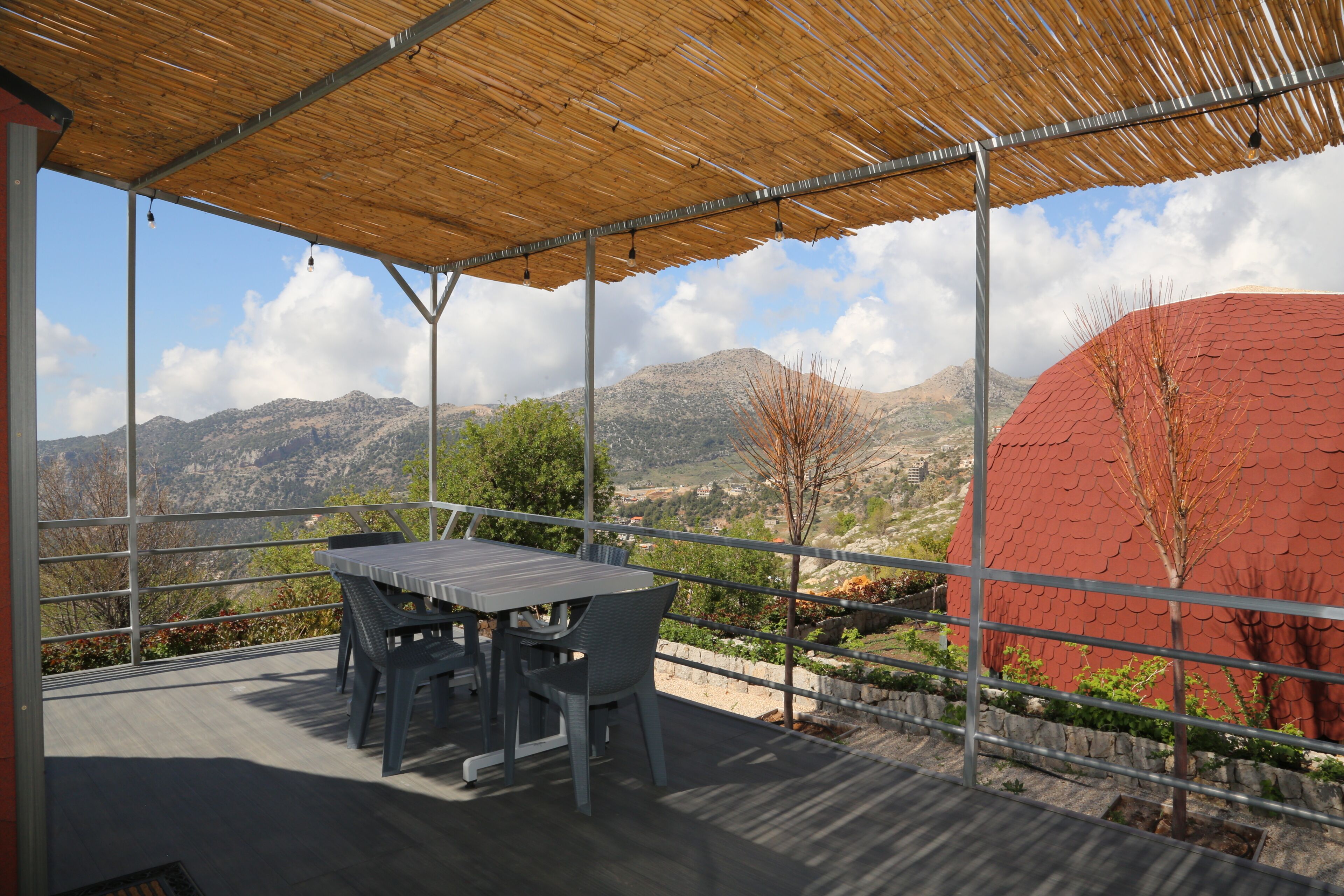 Une terrasse extérieure avec une table et des chaises, un toit en bambou et une vue sur les montagnes.