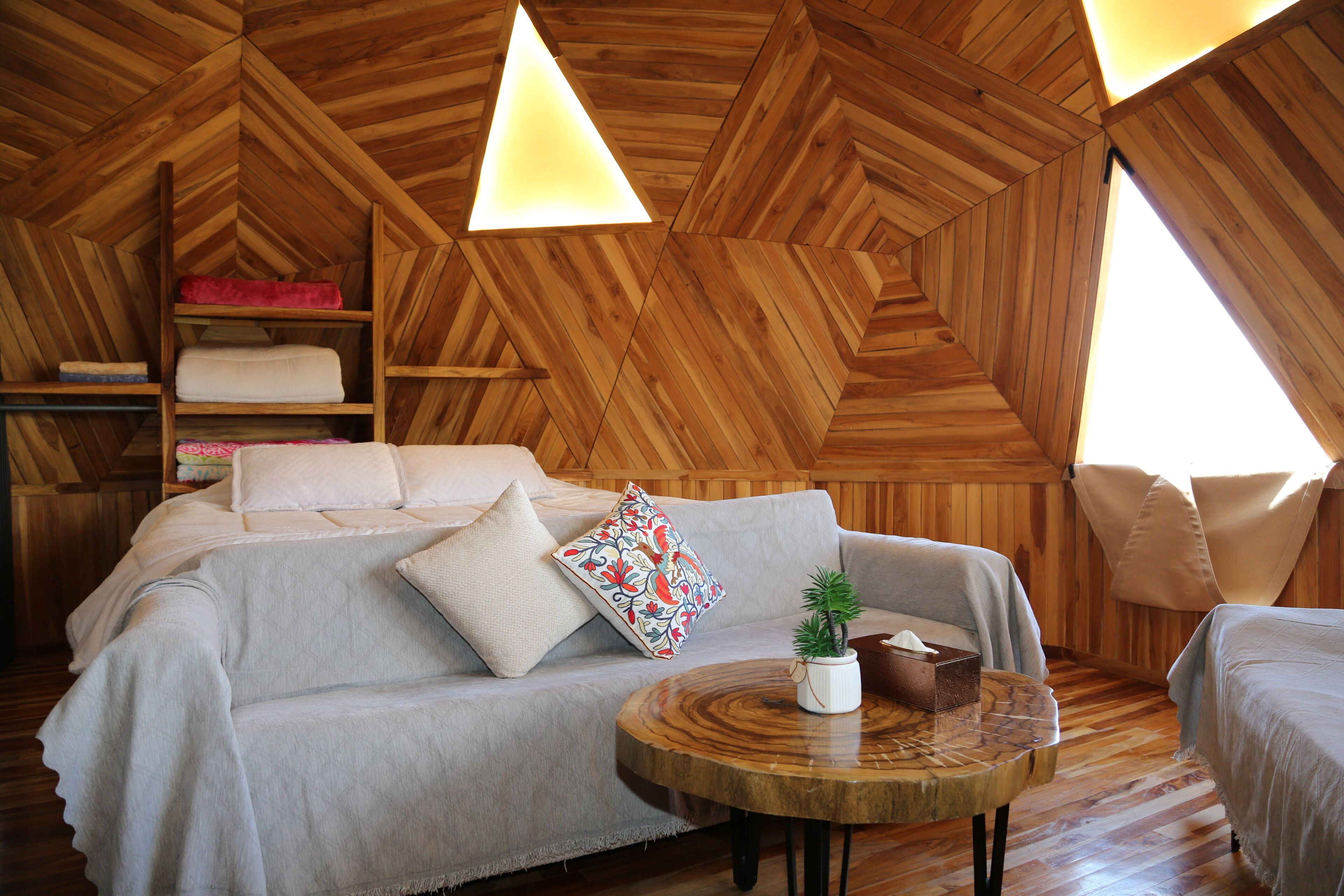 Una habitación acogedora con techo de madera, un sofá, una mesa redonda de madera y una planta pequeña.