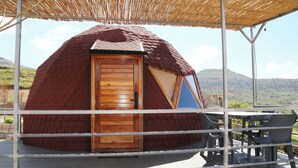 A geodesic dome structure with a wooden door, a covered outdoor seating area, and a view of a hilly landscape. - Sama Tannourine Dome Houses (Tannourine El Faouqa)