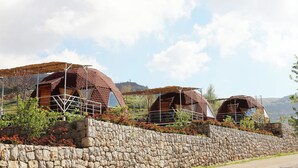 Three dome-shaped cabins with stone walls and wooden roofs, surrounded by a stone wall and vegetation. - Sama Tannourine Dome Houses (Tannourine El Faouqa)