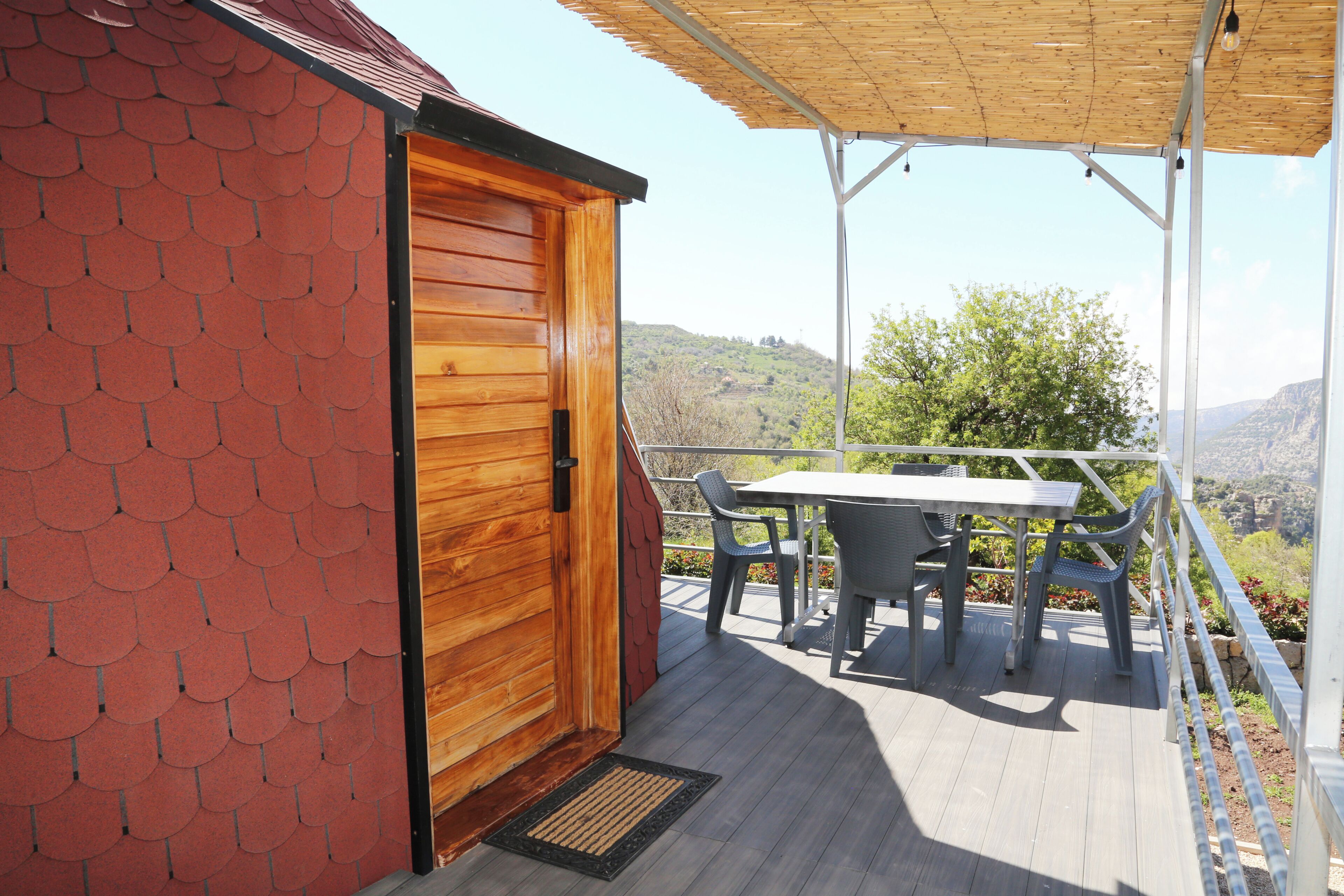 Een houten gebouw met een rode bakstenen muur, een deur en een balkon met een tafel en stoelen.