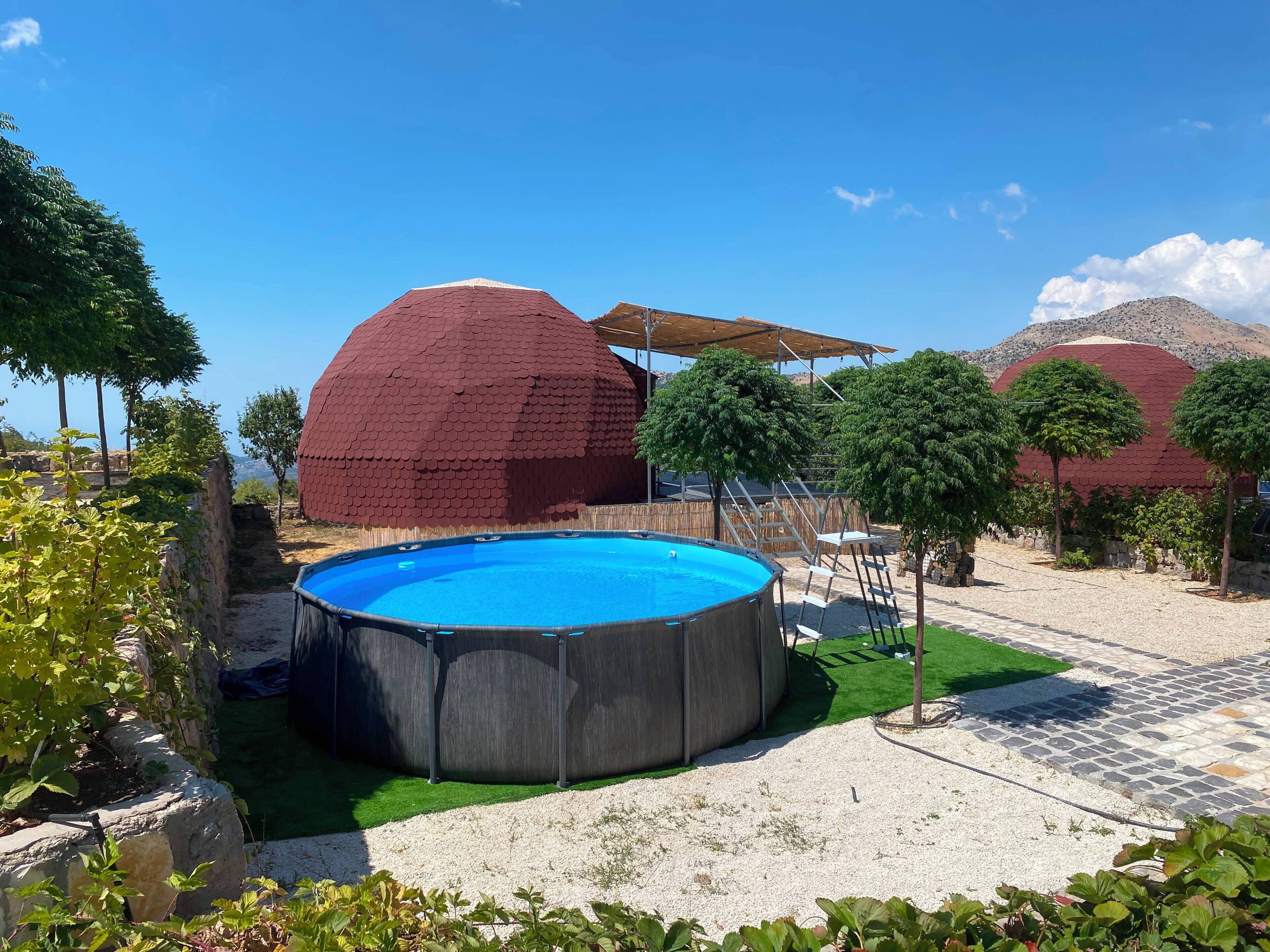 A swimming pool surrounded by a garden with trees and a large dome structure.
