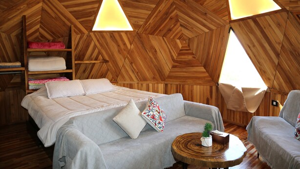 A cozy, wooden-paneled room with a bed, sofa, and a small round table. - Sama Tannourine Dome Houses (Tannourine El Faouqa)