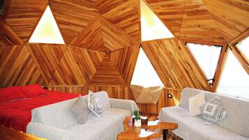A cozy interior with a wooden ceiling, two sofas, a red bed, and a small table with a plant.