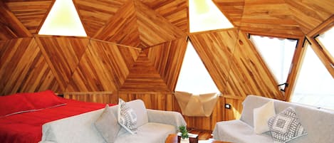 A cozy interior with a wooden ceiling, two sofas, a red bed, and a small table with a plant.