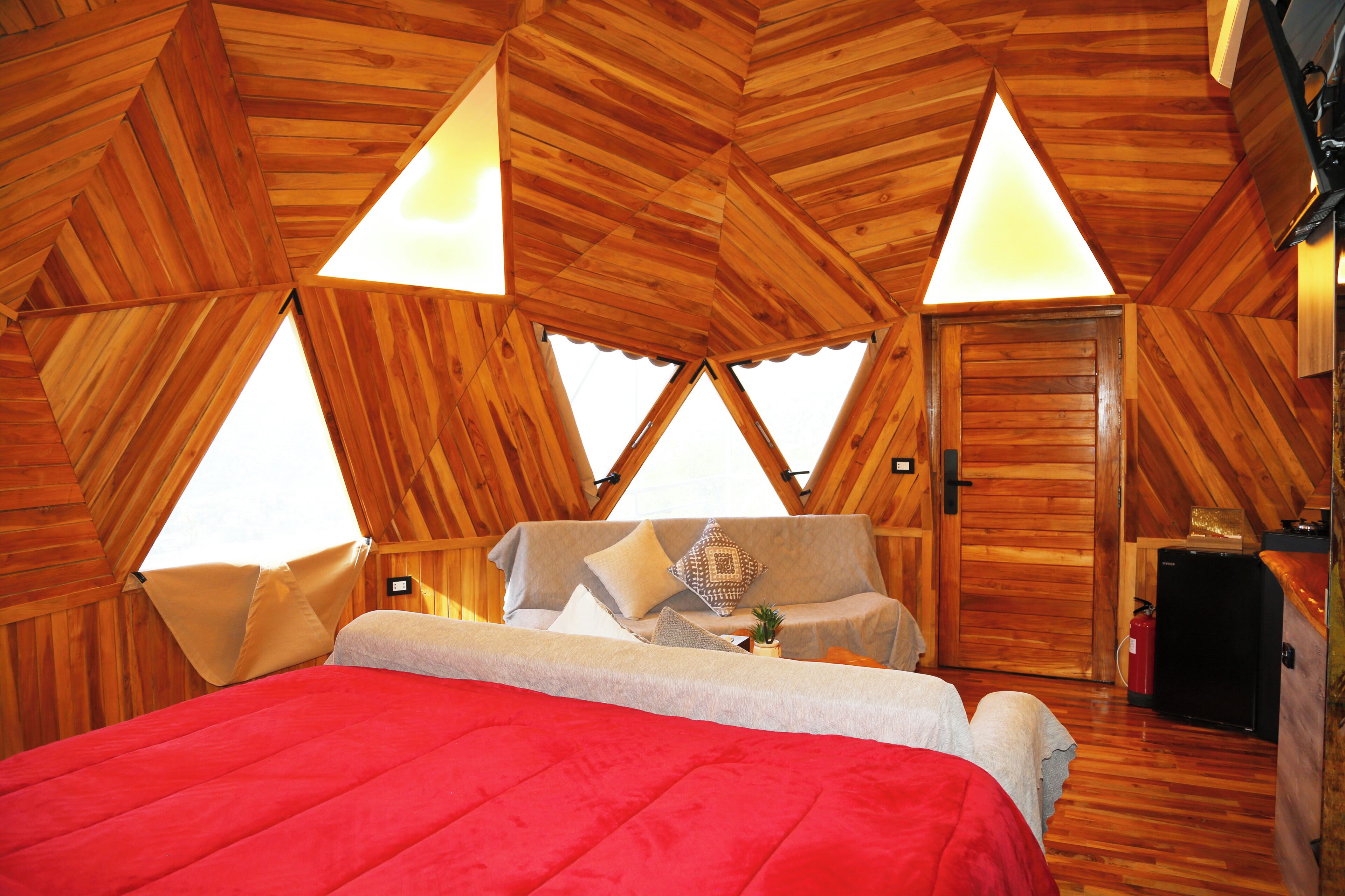 A cozy, triangular wooden room with a bed, a small table, and a door.