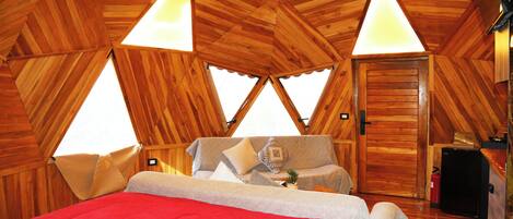 A cozy, triangular wooden room with a bed, a small table, and a door.