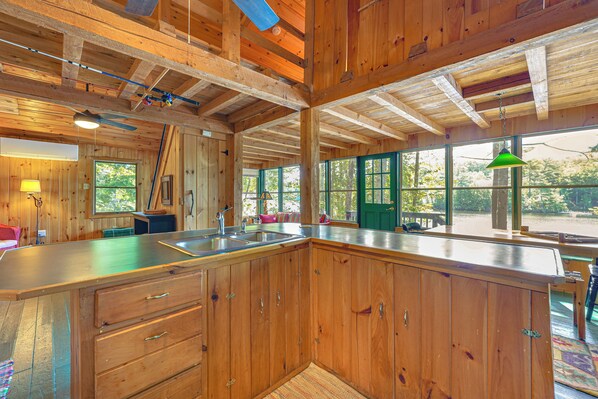L’intérieur d’une cabane en bois comprend un coin cuisine, de grandes fenêtres et un ventilateur de plafond.