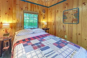 Habitación con paneles de madera, una cama, dos lámparas de noche, una ventana y un ábaco colgado en la pared.