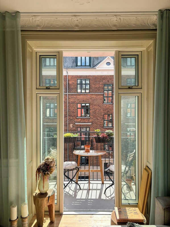 Eine geöffnete Tür, die zu einem Balkon mit Tisch, Stühlen und einem Blumentopf führt.