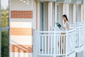 Eine Person steht auf einem Balkon mit einer weißen Brüstung und liest ein Buch.