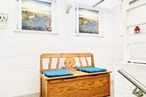 Eine Holzkiste mit blauen Kissen, eine weiße Ziegelwand und zwei gerahmte Bilder.