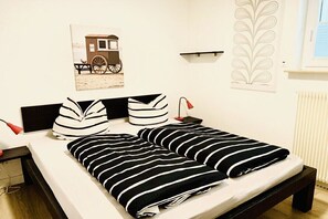 Ein Bett mit gestreifter Bettwäsche, ein Nachttisch mit Lampe, ein Wandregal und ein Bild mit Strandmotiv.