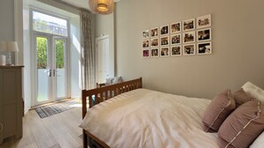 Ein Schlafzimmer mit Bett, Nachttisch, einer Pendelleuchte, einer Tür mit Blick und einer Wand mit gerahmten Fotos.