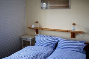 A bedroom with a bed, two bedside tables, a nightstand, a wooden shelf with two lamps, and a framed picture on the wall. - Holiday apartment in Nebel with swimming pool (Nebel)
