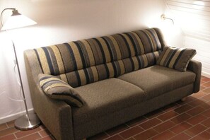 A sofa with striped cushions, a floor lamp, and a tiled floor. - Holiday apartment in Nebel with swimming pool (Nebel)