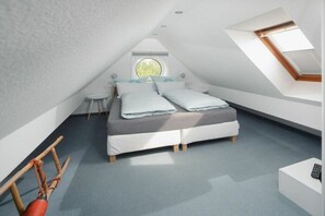 Ein Schlafzimmer mit schrägverdeckter Decke, einem Bett, einem Rundfenster und einem Oberlicht.