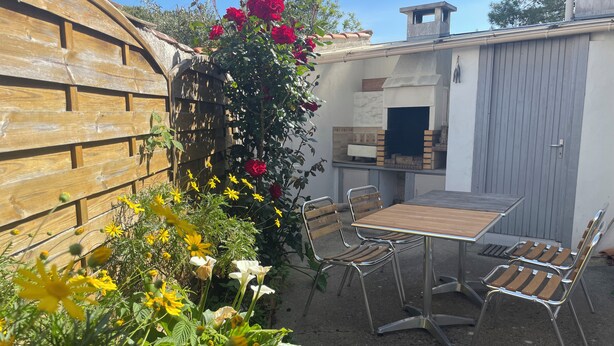 Eine Terrasse mit einem Holztisch und Metallstühlen, umgeben von einem Garten mit verschiedenen Pflanzen und Blumen.