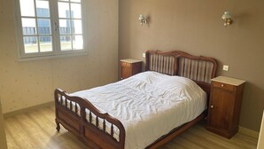 Ein Schlafzimmer mit einem hölzernen Bett, zwei Nachttischen, einer Fensterbank und einer Wandleuchte.
