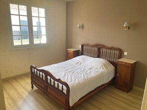 Un dormitorio con una cama de madera, dos mesitas de noche, una lámpara de pared y una ventana con vistas.