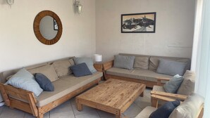 Ein möbliertes Wohnzimmer mit einer Couch, einem Holztisch, einem Holzstuhl, einem runden Spiegel und Wandleuchten.