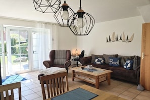 A living room with a sofa, armchair, coffee table, and pendant lights. - What luck! - with a fence (Neßmersiel, Ostfriesland, Nordsee)