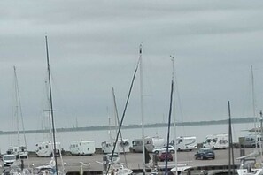 Ein Yachthafen mit vertäuten Booten und Wohnmobilen, im Hintergrund ein Gewässer und ein bewölkter Himmel.