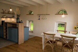 A kitchen with wooden cabinets, a dining table, and chairs. There are hanging lights and a window with a view of greenery. - Holiday apartment with 1 bedroom (Versmold)