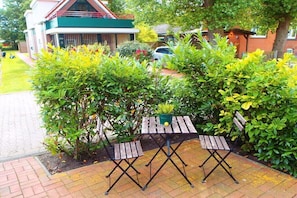 Eine Terrassenfläche mit einem Holztisch und zwei Stühlen, umgeben von üppiger Vegetation.