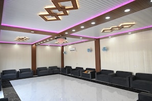 A conference room with a marble floor, black sofas, wooden paneling, and modern ceiling lighting. - BANARAS BLOSSOM RESORT (Varanasi)