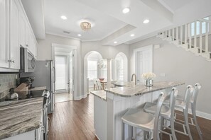 A modern kitchen with white cabinetry, a marble countertop, and a central island with bar stools. - Balcony on Every Floor | Walk to Sand + Lagoon Pool | 30A Emerald Waters (Inlet Beach)