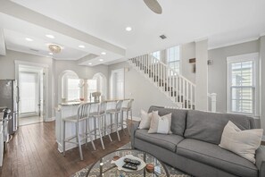 A spacious living room with a grey sofa, a coffee table, and a staircase leading to an upper floor. - Balcony on Every Floor | Walk to Sand + Lagoon Pool | 30A Emerald Waters (Inlet Beach)