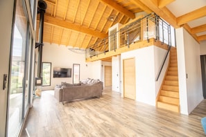 A spacious living area with a wooden floor, a sofa, a staircase, and a balcony with a railing. - Chalet Lignum, Sauna & SPA, Near Ski Slopes (La Bresse)