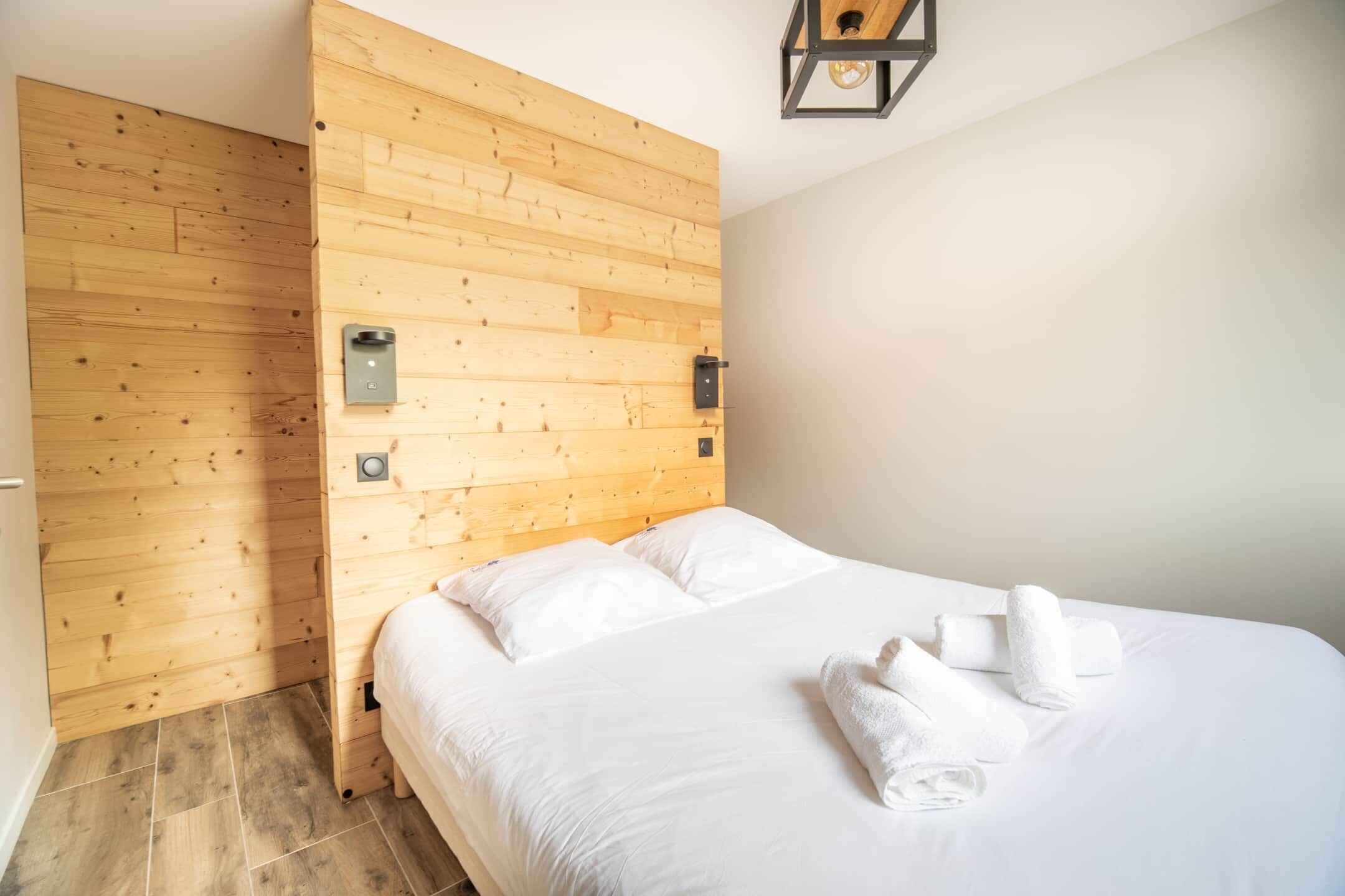 A hotel room with a wooden headboard, a bed with white linens, and a wall-mounted light fixture.
