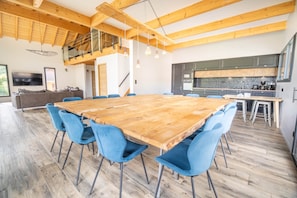 A spacious room with a large wooden dining table surrounded by blue chairs, a kitchen area with modern appliances, and a loft with a wooden ceiling. - Chalet Lignum, Sauna & SPA, Near Ski Slopes (La Bresse)