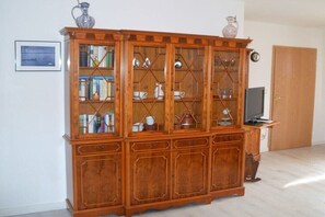 Ein Holzkabinett mit Glastüren, das Küchenutensilien und einen Fernseher beherbergt.