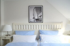 Ein Schlafzimmer mit zwei Betten, einem Kopfteil, Nachttischen und einem gerahmten Bild an der Wand.