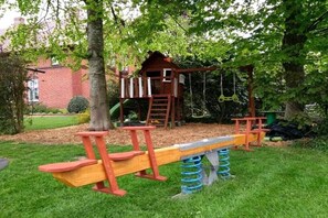 A playground with a swing set, a seesaw, and a climbing structure. - Holiday home with 2 bedrooms (Großefehn)