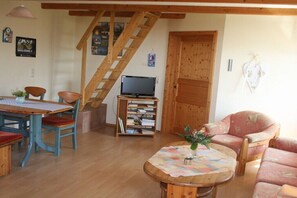 A living room with a wooden staircase, a television, a bookshelf, a dining table with chairs, and a sofa. - Holiday home with 2 bedrooms (Großefehn)